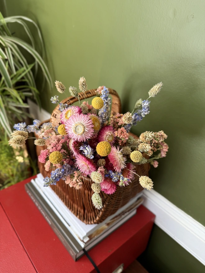 a bouquet of dried flowers in bright colours displayed in a wicker basket against a green wall
