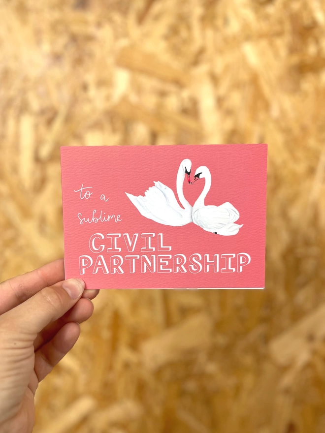 a greetings card with a deep pink background featuring two swans with their necks meeting in a heart shape, and the phrase “to a sublime CIVIL PARTNERSHIP”
