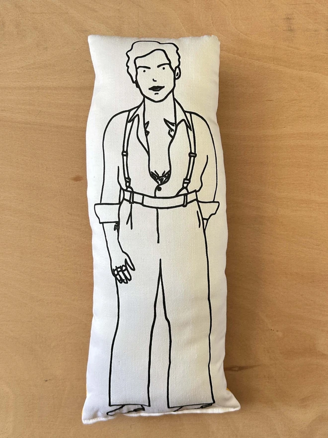 Black and white screen printed cushion featuring an illustration of Harry Styles, on a plain wooden table.