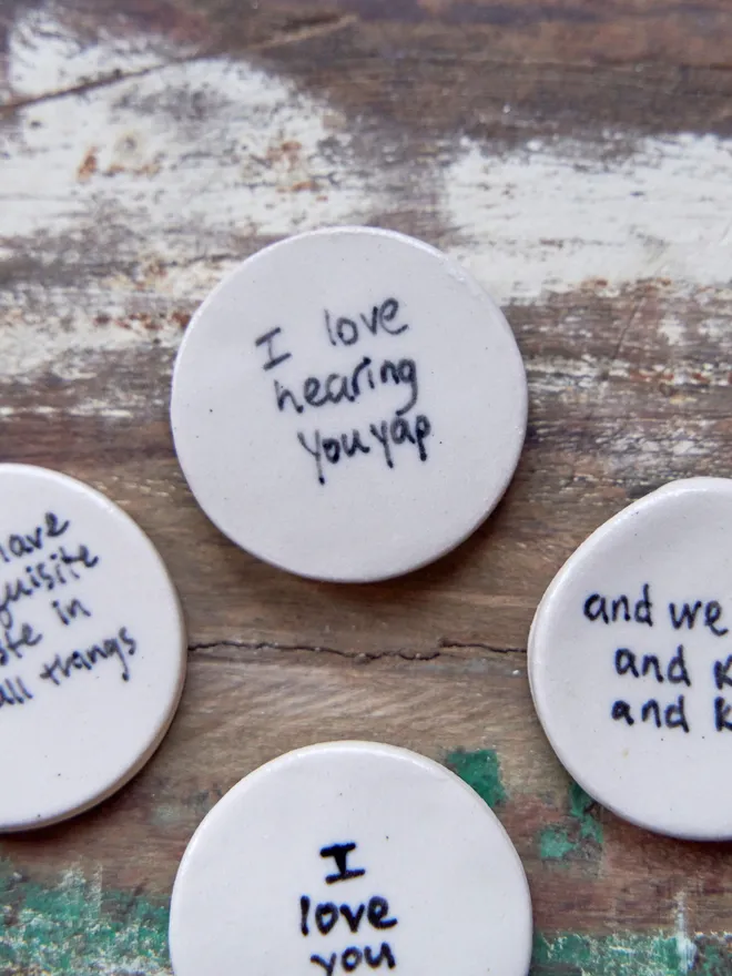 Small ceramic love token. Ceramic love tokens with phrases written on them in black on a wooden surface