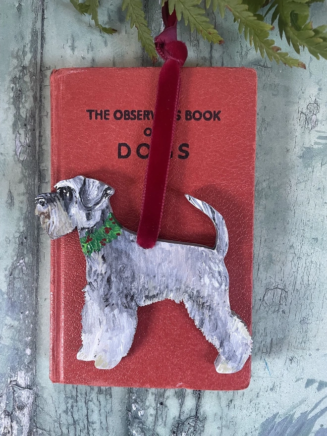 Miniature Schnauzer Hand - Painted Christmas Decoration hung with red velvet ribbon and placed on a red book about dogs