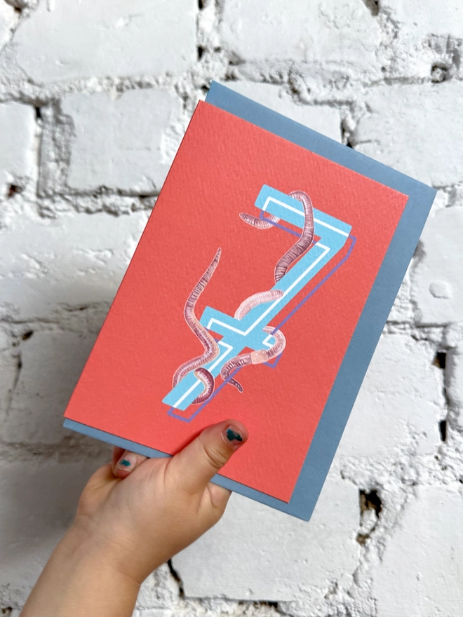 a bright red card with a big blue number 7 and some illustrated earthworms with a blue envelope