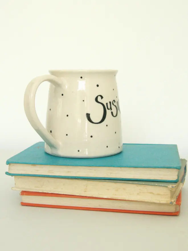 large personalised hand-thrown ceramic mug. mug photographed from the side, placed on top of a pile of books.