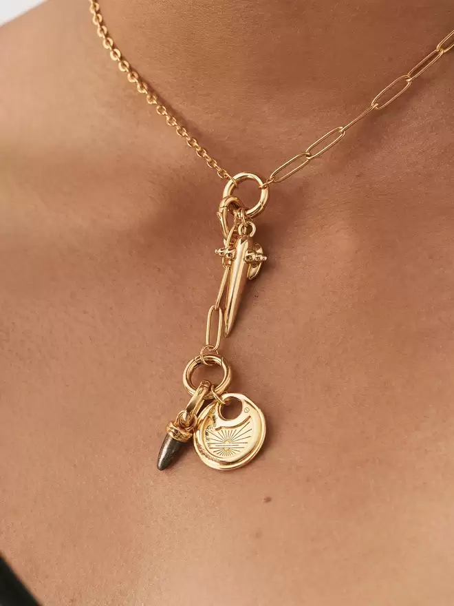 woman wearing a gold necklace with a dagger pendant, hematite bullet charm and pancake lock medallion