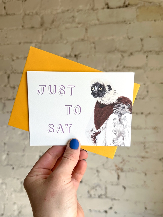  a greetings card featuring an illustration of a Coquerel’s Sifaka with the text “just to say” with a deep yellow envelope