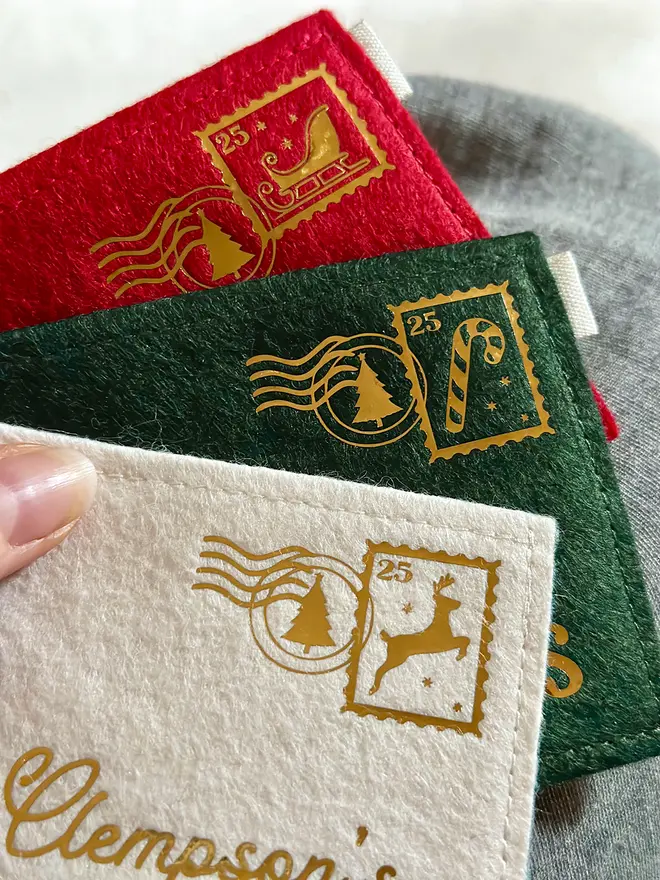 Three handmade felt envelopes, in red, green, and white with golden Christmas stamps and postmarks in the top right corners.
