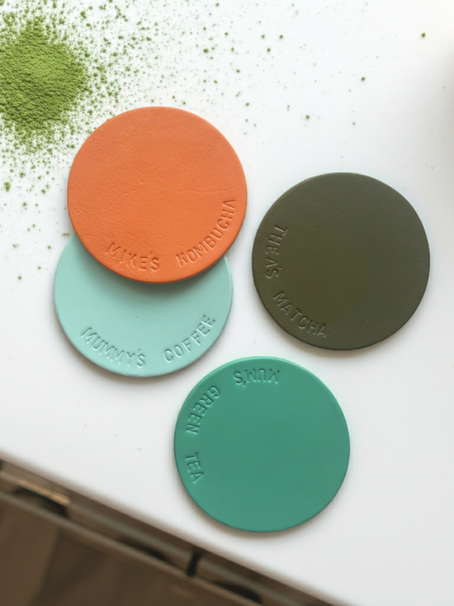 4 leather coasters stamped with different personalised text, on a white back ground with spilled matcha powder.