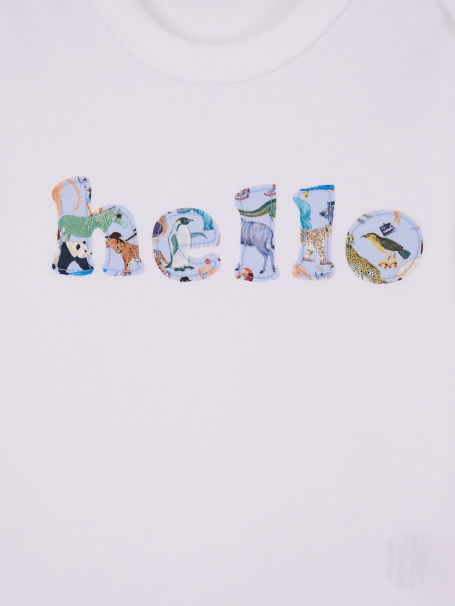 a close up of a white cotton romper with hello sewn onto it in a liberty zoo animal print. close up of the appliqué stitching