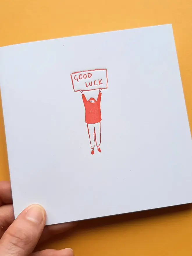 'Good Luck' Letterpress Handprinted Greetings Card, person holding white good luck card with an orange design against a yellow background. 