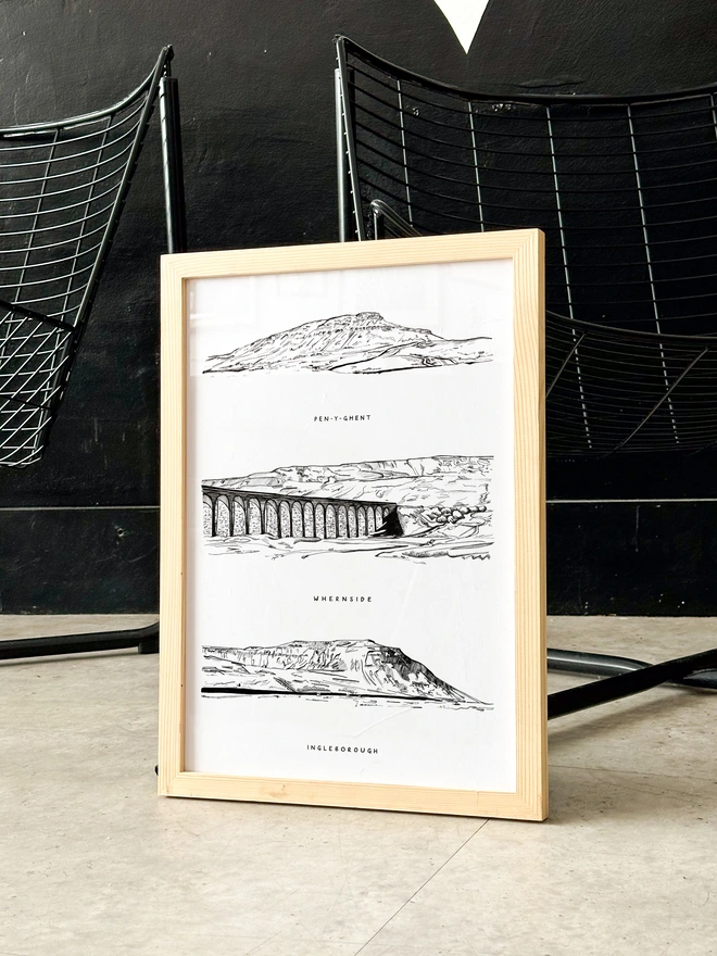 print featuring black and white line illustrations of the yorkshire three peaks, framed and leaning against a chair