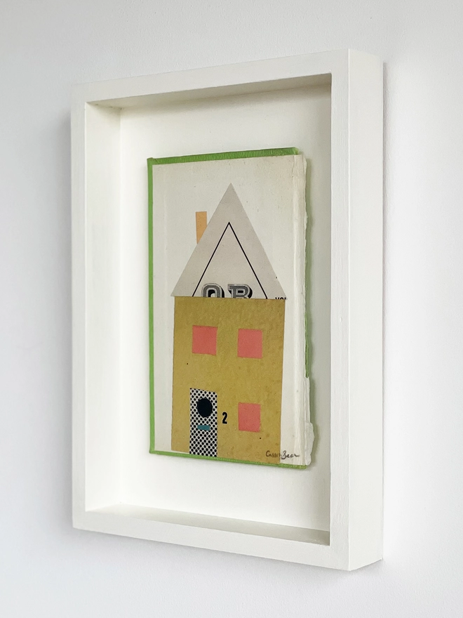 An angled view of a mustard yellow house portrait on a vintage book cover. Float mounted within a hand painted wood box frame.