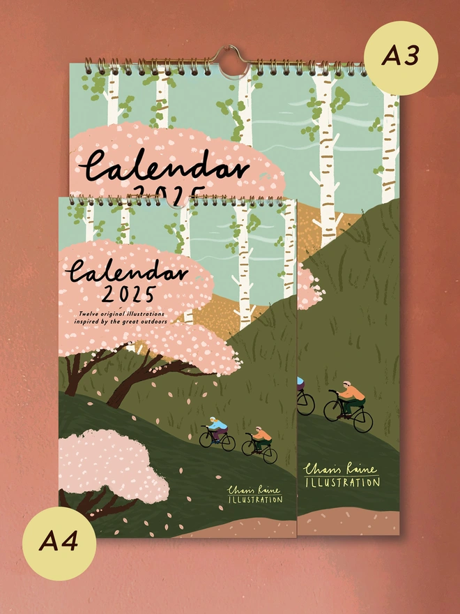 An image showing the difference in A4 and A3 sizing. A4 is half the size of A3. The calendar is beautifully illustrated showing 2 cyclists going uphill surrounded by cherry blossom.