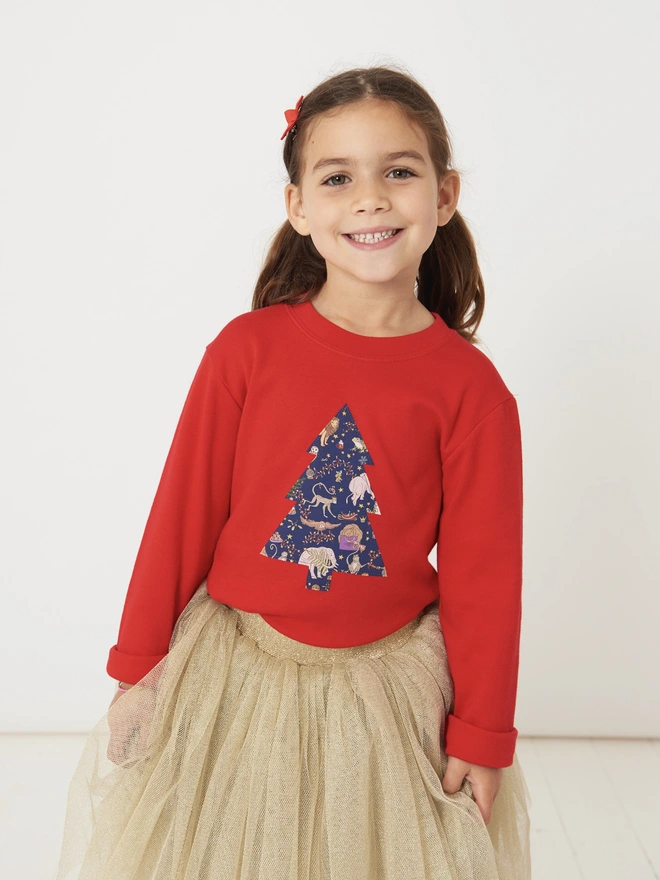 a 4 year old girl wearing a red t-shirt with a christmas tree cut from Liberty Christmas print sewn onto the front