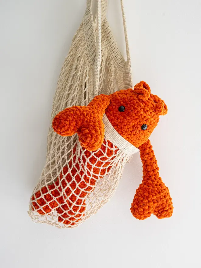 Chunky Chenille Cuddly Crochet Crustacean Lobster Plush, an orange lobster plush hanging from a bag against a white backdrop. 