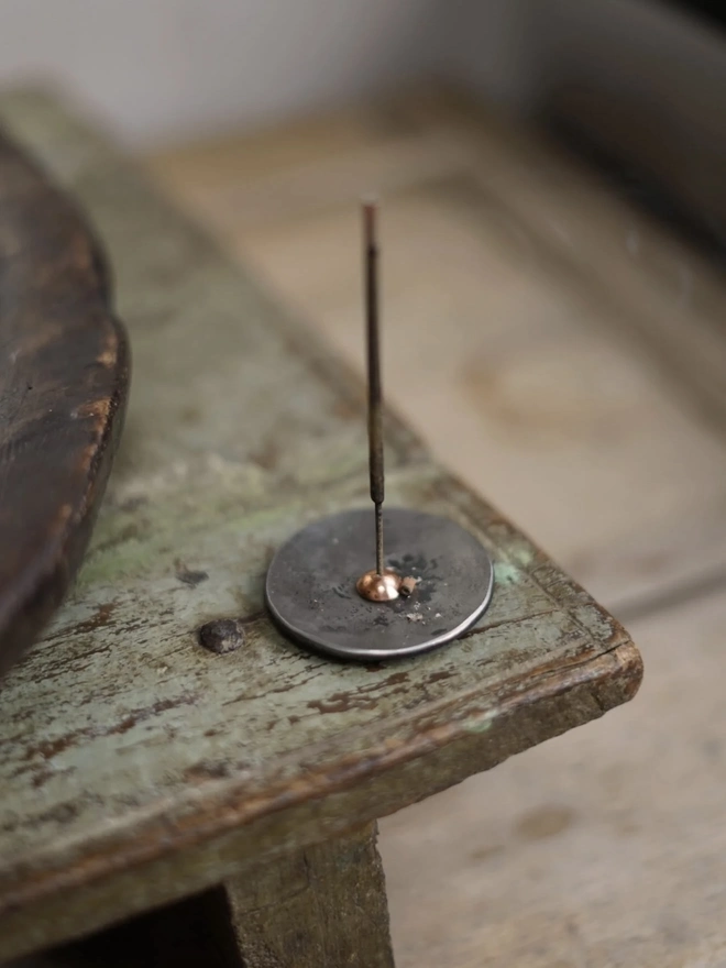 Copper And Steel Incense Holder, a metal incense holder sitting on a wooden surface in a workshop. 