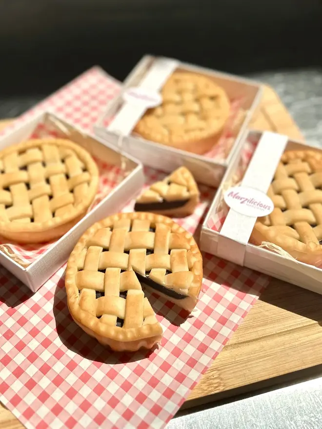 Marzipan Cherry Pie, a group of marzipan cherry pies on a traditional picnic cloth. One is placed next to a group that are packaged. 