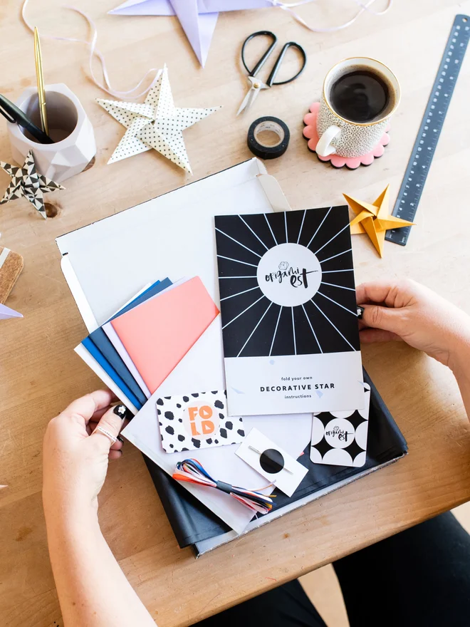Woman holding origami kit with origami stars scattered on table