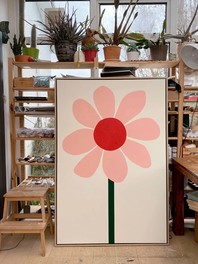 Large painting of a flower leaning against shelves in artists studio