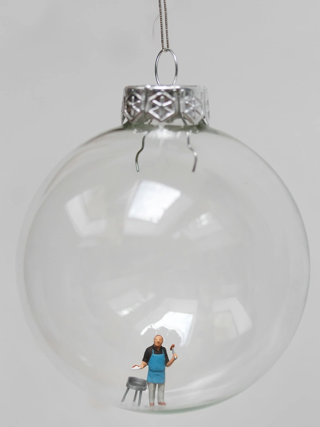 Miniature figure of a man barbecuing, in a glass Christmas bauble 
