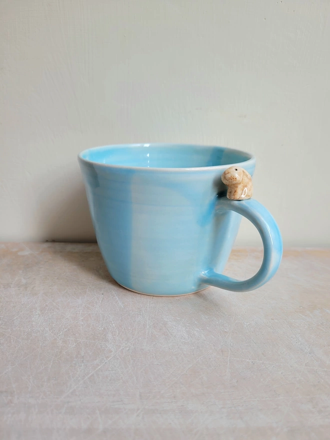 Blue pottery cup with a brown ceramic lop ear rabbit perching on the handle 