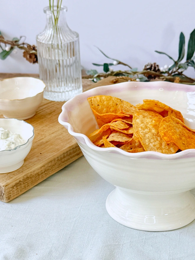 Undulating hand thrown porcelain stem bowls with satin cream glaze and pink or turquoise rim on a rustic table top