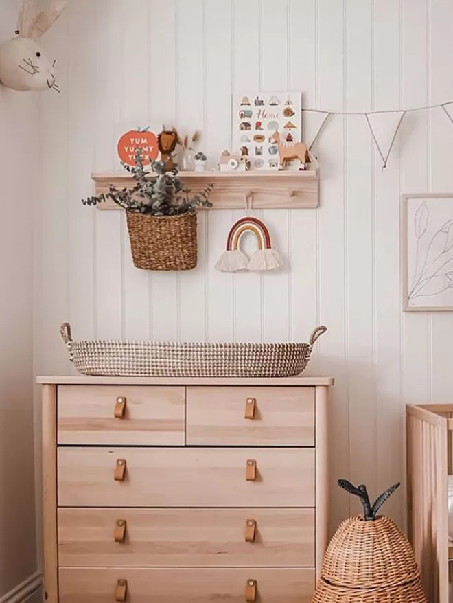 A beautiful neutral nursery, with a solid wood pegrail shelf decorated with kids room decor, hung over a babies changing table 