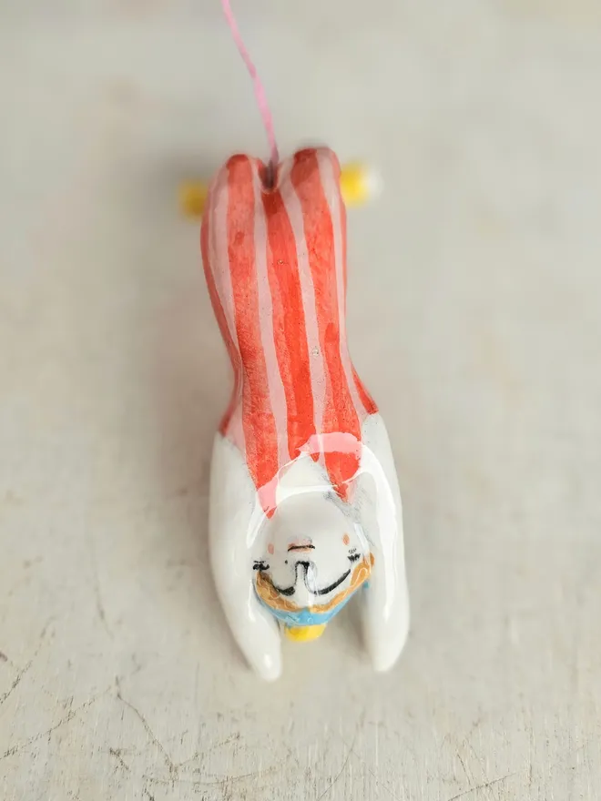 female acrobat hanging upside down in a red and pink stripe suit, lying down front view
