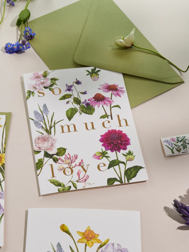 'so much love' illustrated floral card. a white floral card and green envelope photographed against a plain background. 