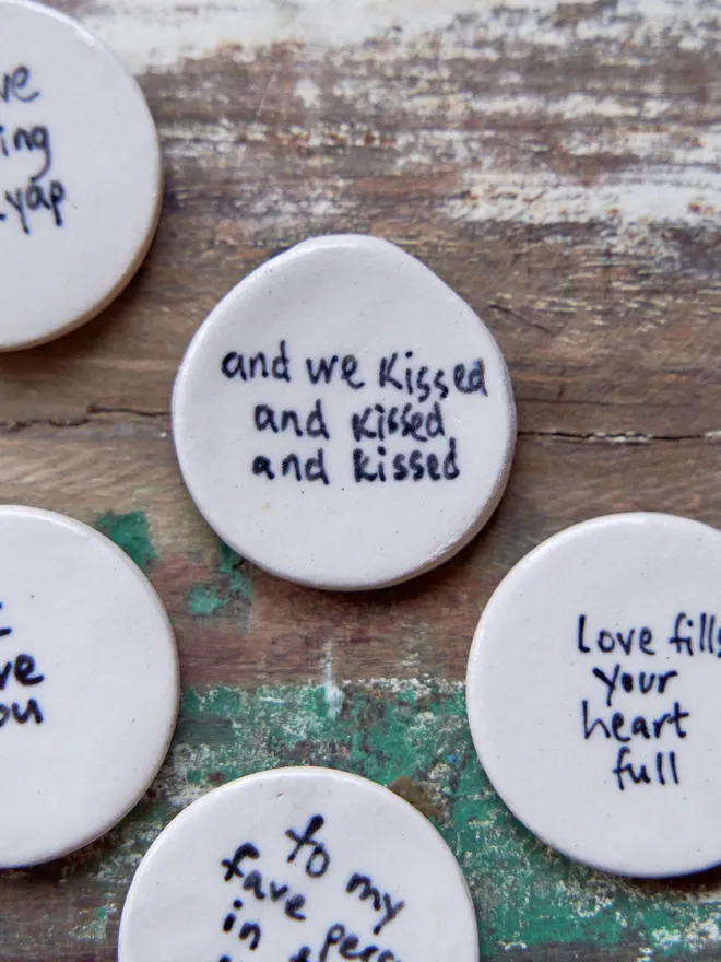 Small ceramic love token. Ceramic love tokens with phrases written on them in black on a wooden surface
