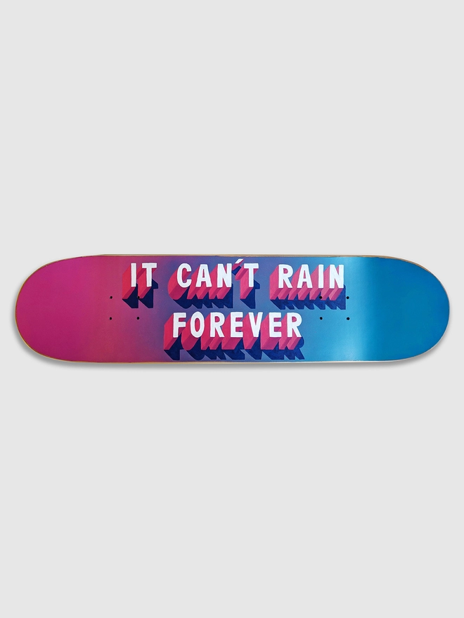 A skateboard that has a spray painted pink and blue background and 3d typography that reads It Can’t Rain Forever in pink and white.