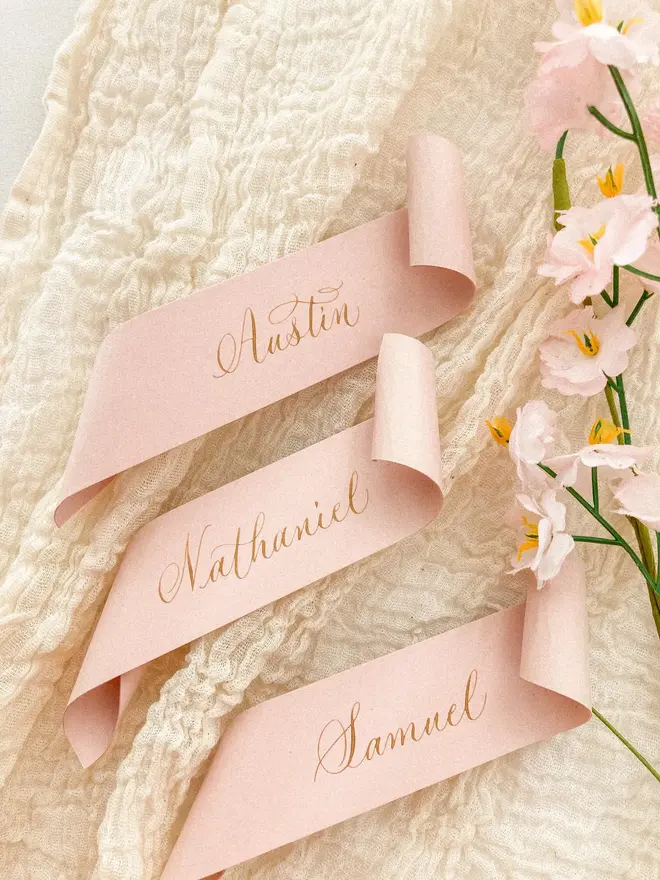 blush pink scroll calligraphy wedding place cards. pink scrolls on muslin background.