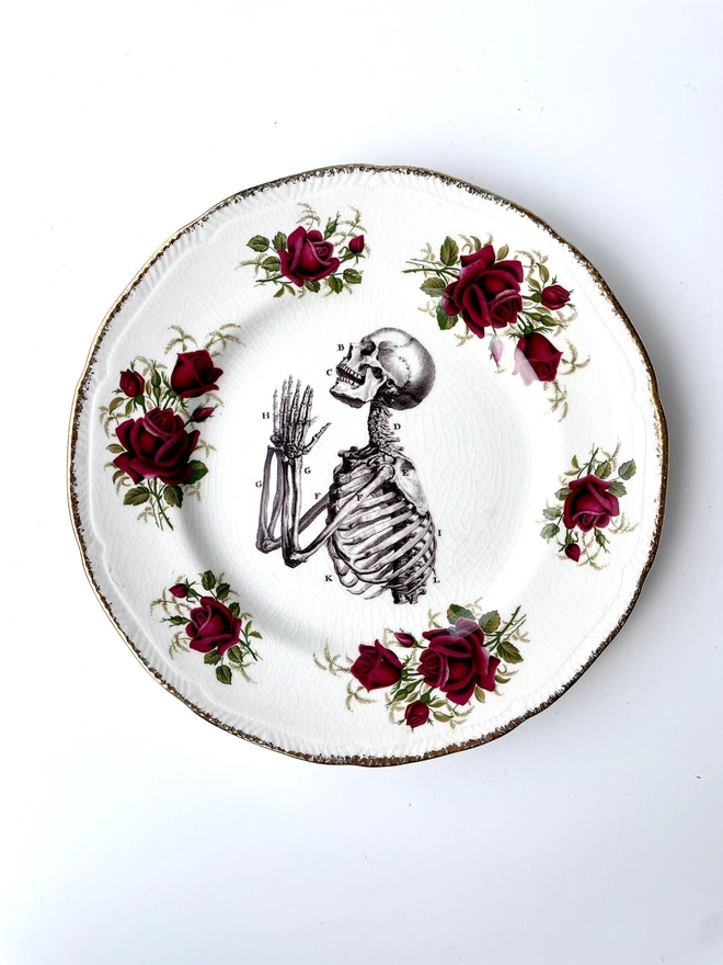 vintage plate with an ornate border, with a printed vintage illustration of a praying skeleton in the middle 