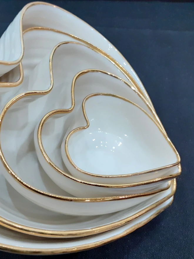 porcelain heart shaped bowl. five nesting white heart shaped bowls with gold rims stacked inside each other.