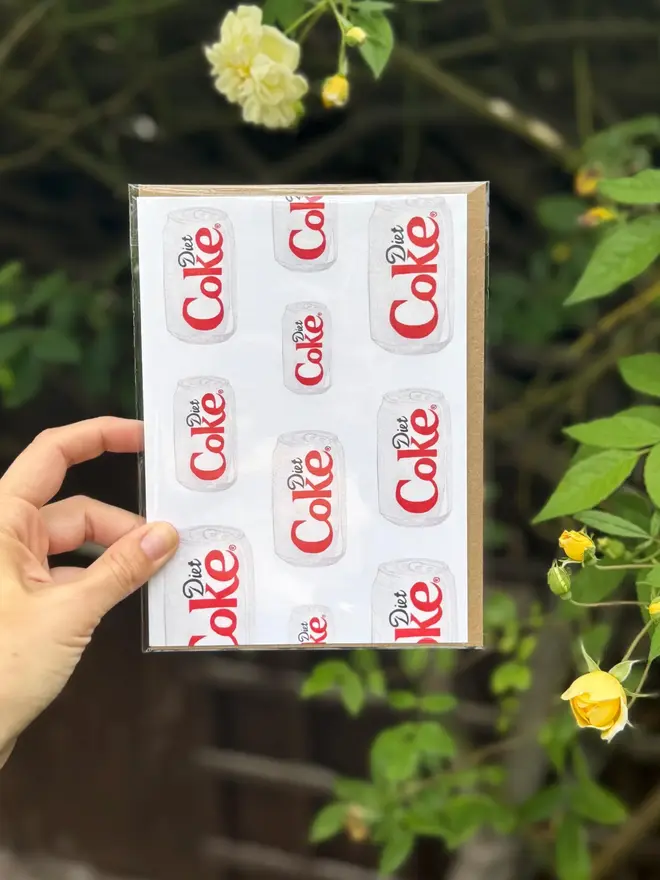 diet coke cans illustrated card. card photographed against leaves and flowers backdrop.