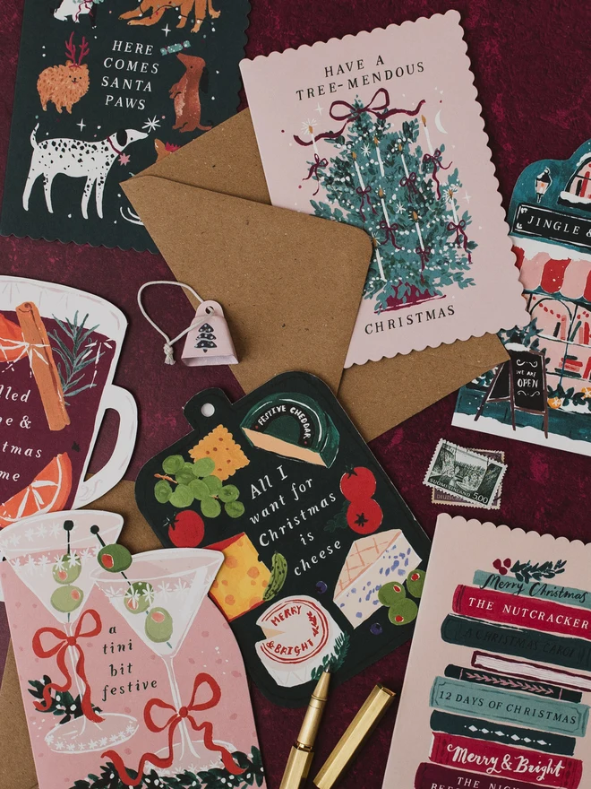 Bookish Christmas card on a burgundy background with the Santa Paws, Tree-mendous, Cheeseboard and Tini Bit Festive Christmas cards