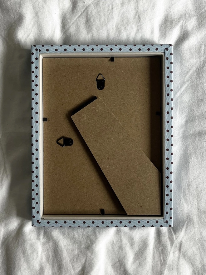 Blue & Burgundy Pembroke Dot Frame, the back of a colourful dotted frame sitting on a plain white surface. 