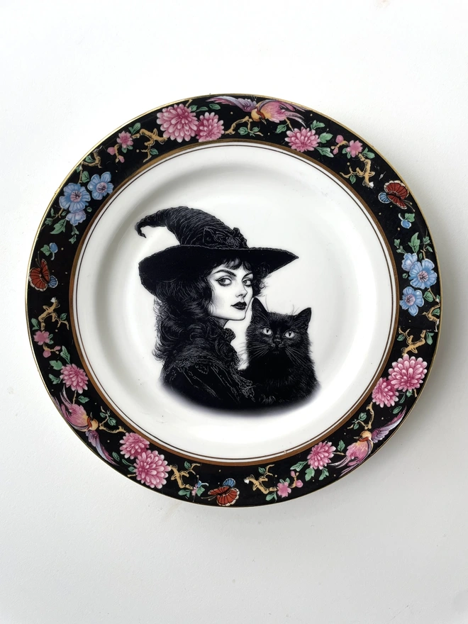 vintage plate with an ornate border, with a printed vintage illustration of a Victorian witch and her black cat in the middle 