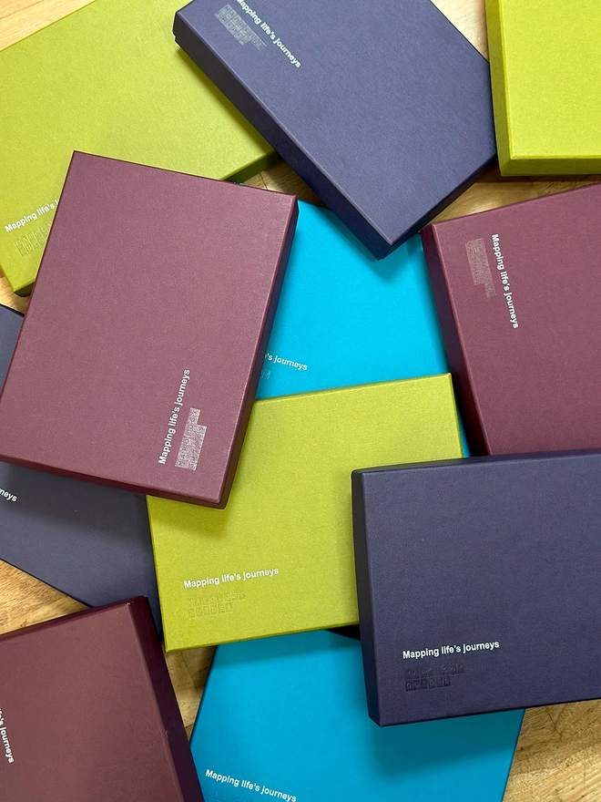 Branded boxes in olive green, kingfisher blue, aubergine and plum