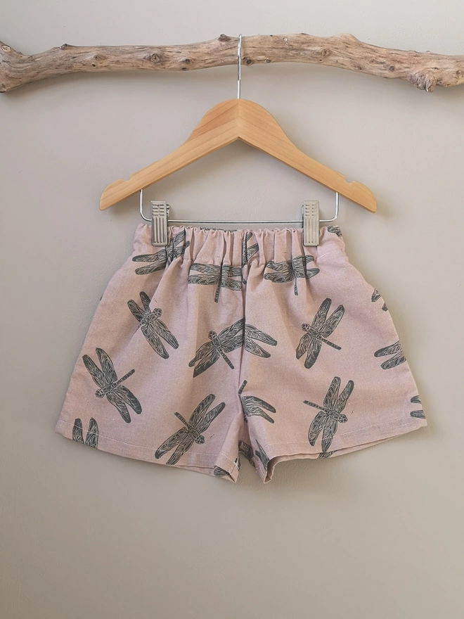 Pink cotton linen lightweight unisex childrens shorts. Featuring a delicate grey dragonfly print. Simple design with elasticated waist and side seam pockets. 