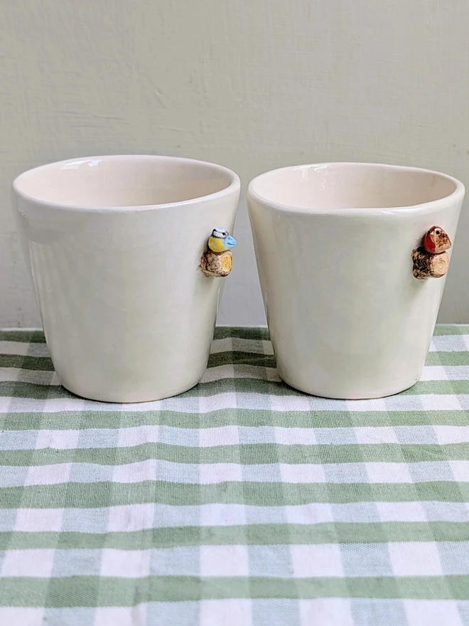 robin and blue tit espresso coffee cups with a tiny handmade bird resting on a small ceramic wooden tree branch in white earthenware pottery