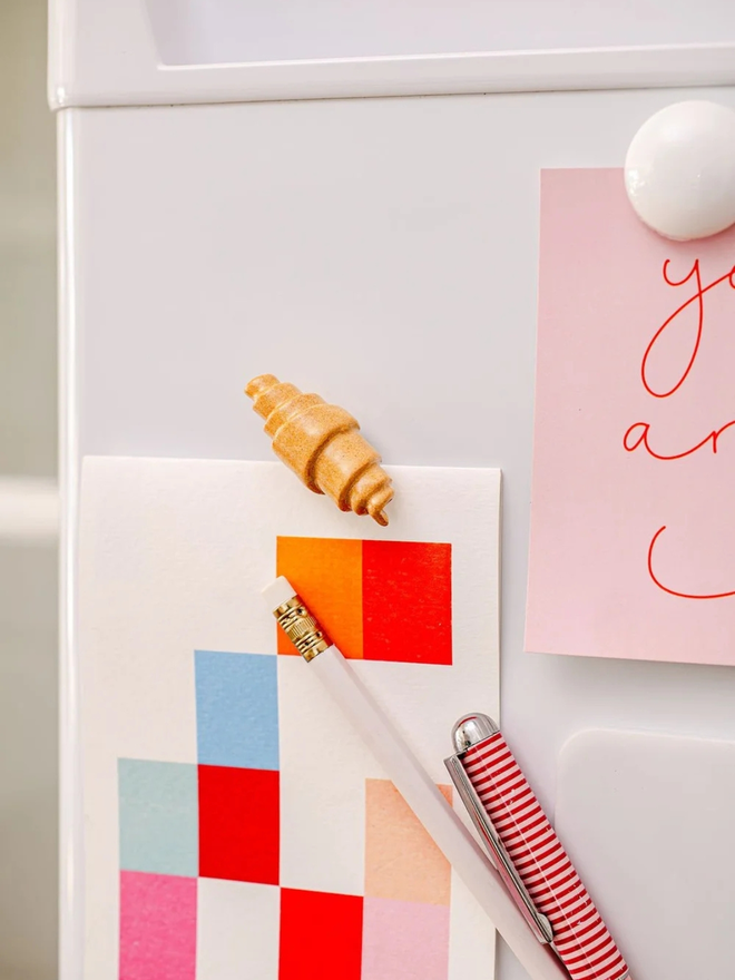 ceramic pastry magnets. a ceramic croissant magnet on a fridge door.