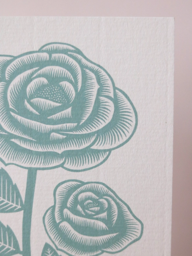 A greetings card feature a teal rose design based on an original linocut print