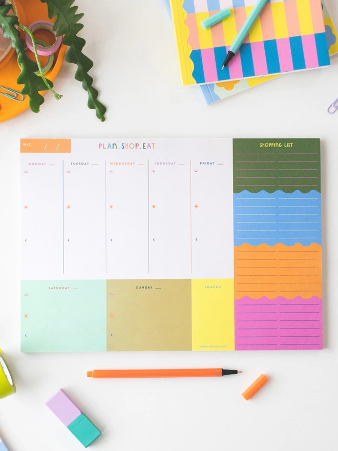Colourful flatlay on desk of the Raspberry Blossom plan, shop, eat weekly planner notepad with tear off shopping list