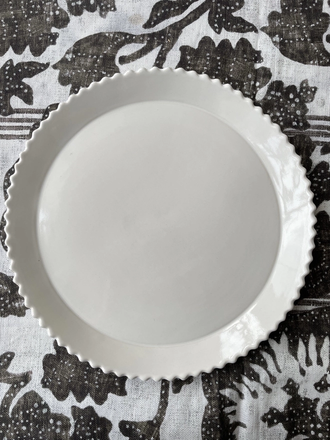 white scalloped edge dinner plate on a black and natural linen cloth