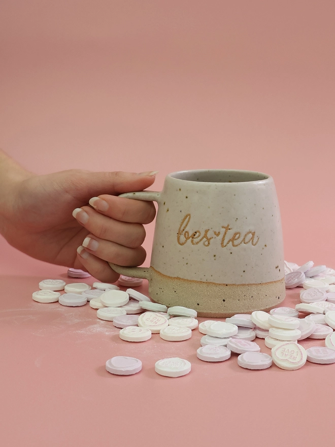 hand holding a large handmade white ceramic mug with the saying bes-tea (a pun on bestie) on the front