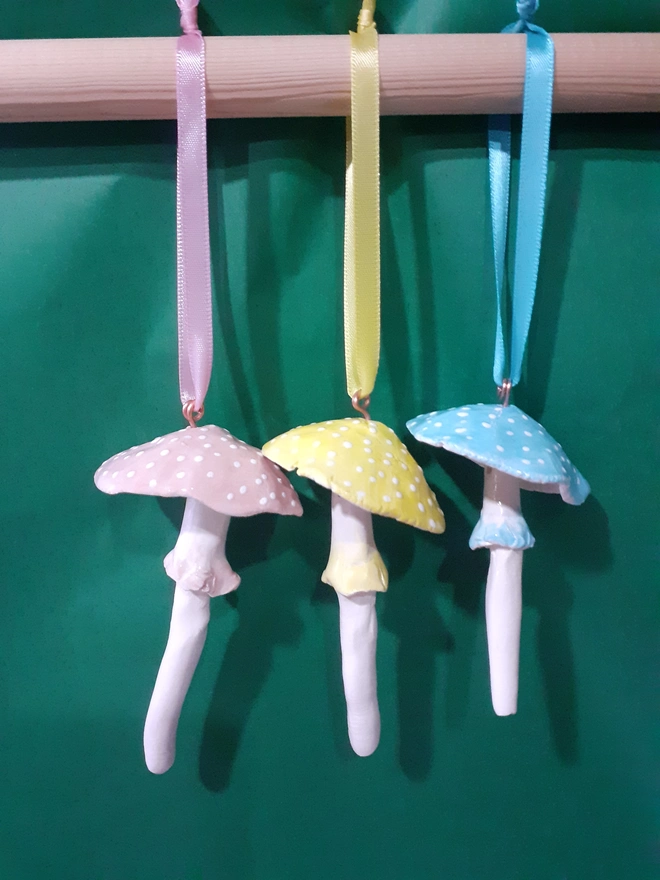 Set of three handmade ceramic pastel toadstool hanging decorations with pink, yellow and blue caps, white polka dots and satin ribbon hangers.