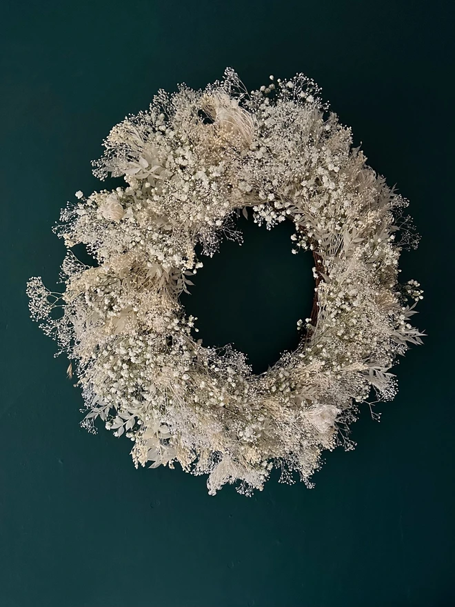 dried floral white door wreath. a circular white and green wreath made of dried flowers hung on a forest green wall.