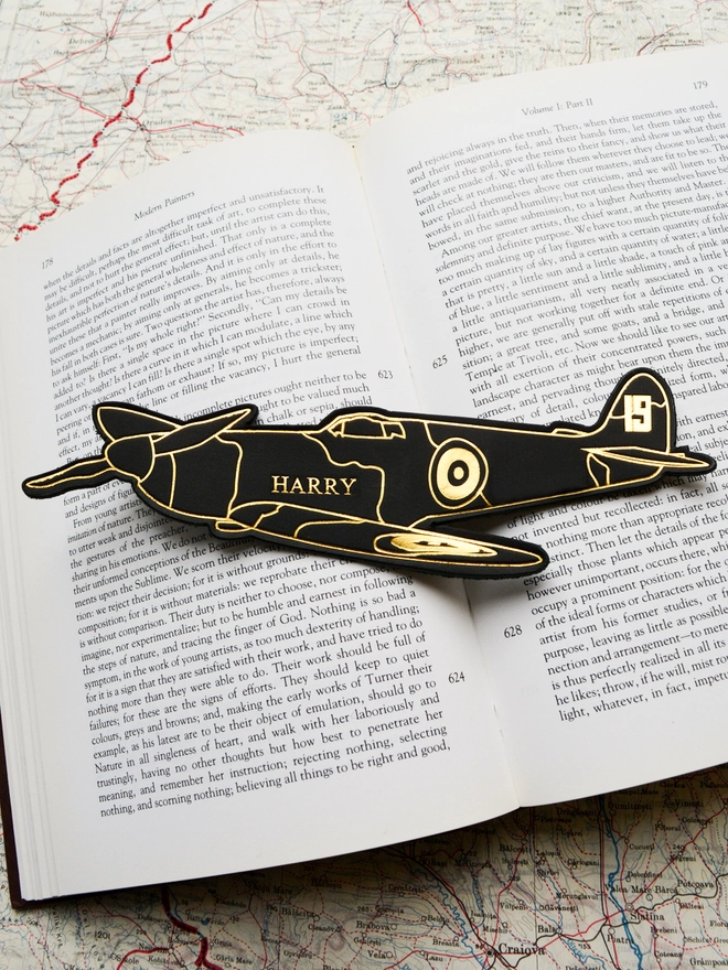 a black leather spitfire airplane bookmark with gold personalization of a name on the main body by Natthakur