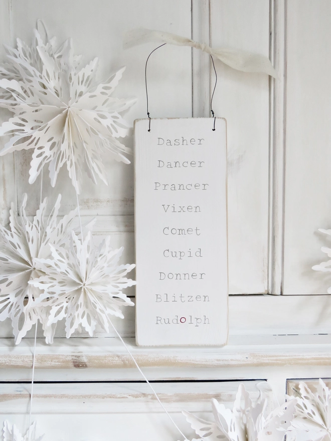 white painted wooden sign with reindeer names strung with wire and decorated with ribbon