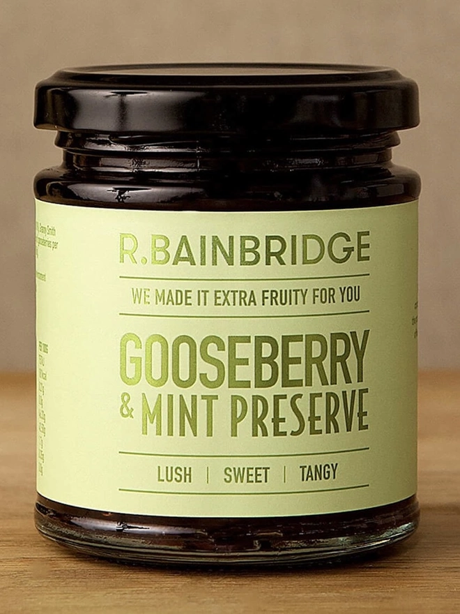 Gooseberry & Mint Chutney (Set Of 1, 2 Or 3), a jar of jam sitting on a wooden surface against a plain backdrop. 